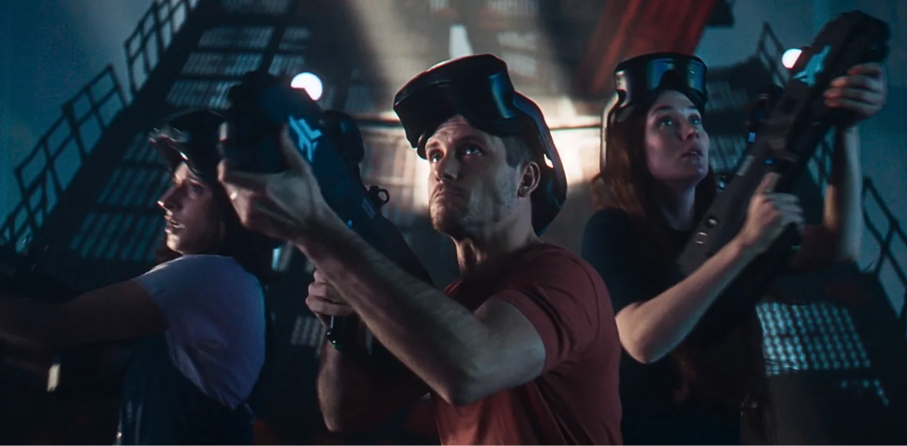 Players in VR headsets hold their weapons ready
